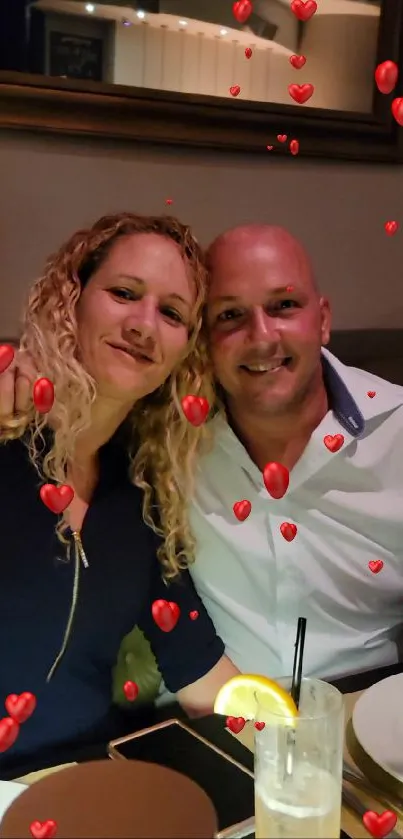 Couple smiling with red heart overlay in a cozy dining setting.