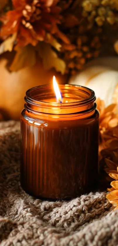 Glowing candle with autumn decor on cozy knit surface.