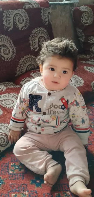 Adorable baby sitting on a cozy patterned sofa indoors.