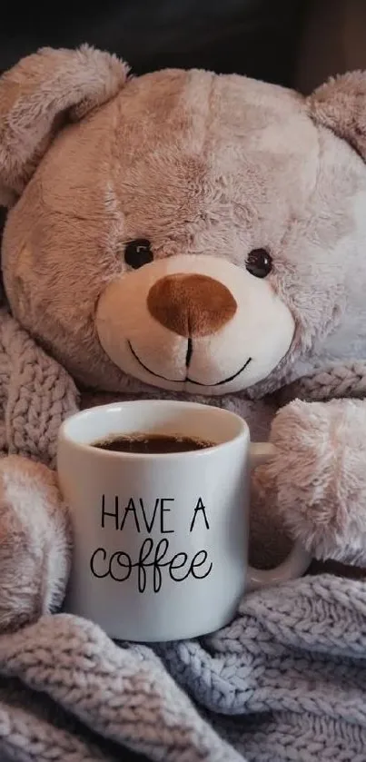 Teddy bear with coffee mug wrapped in a knitted blanket.