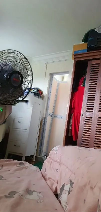 Cozy bedroom with pink bedding and a standing fan.