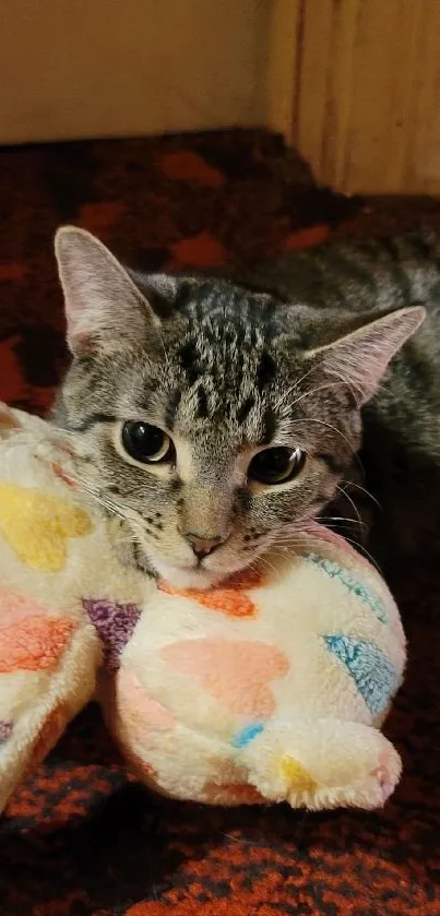 Tabby cat cuddling a plush toy on a red carpet.