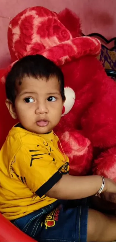 Child sitting with red teddy bear in chair.