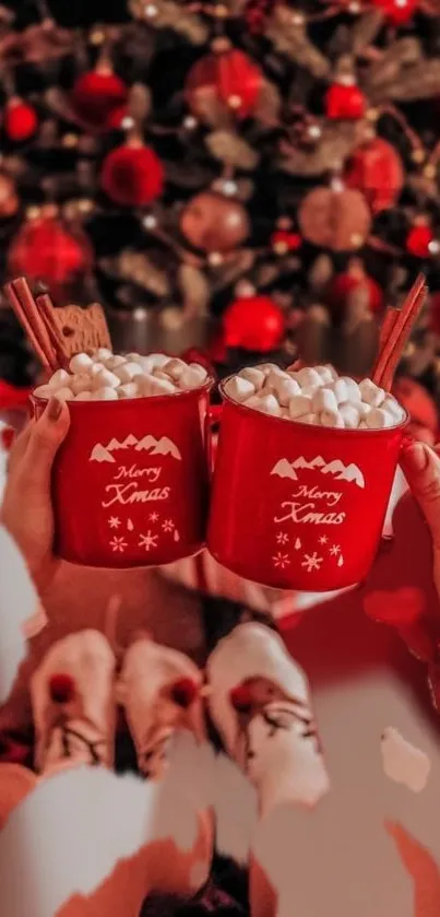 Two red mugs with marshmallows by a Christmas tree.