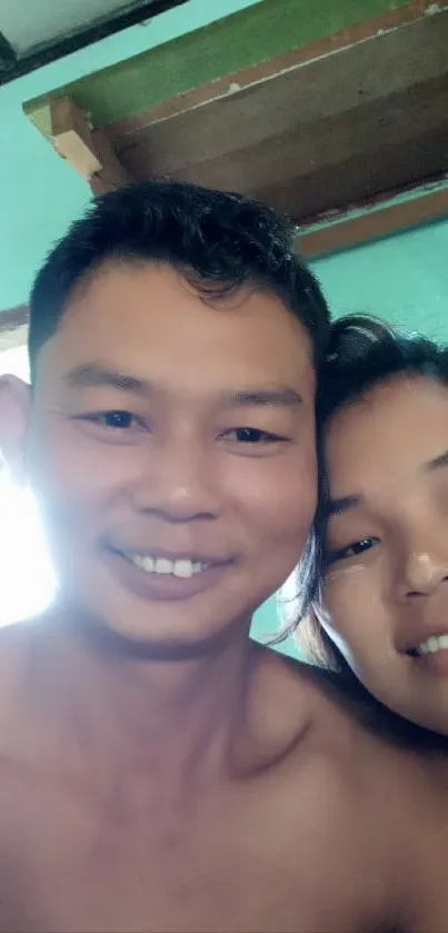 Smiling couple indoors with teal walls and wooden ceiling.