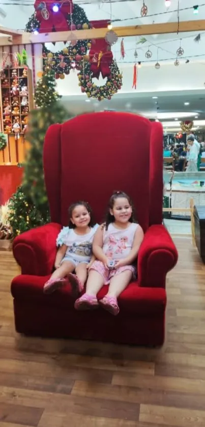 Two children on a festive red chair with Christmas decor.