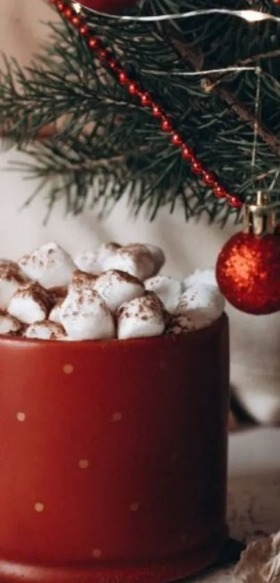 Red mug of hot cocoa with marshmallows beside Christmas tree decorations.