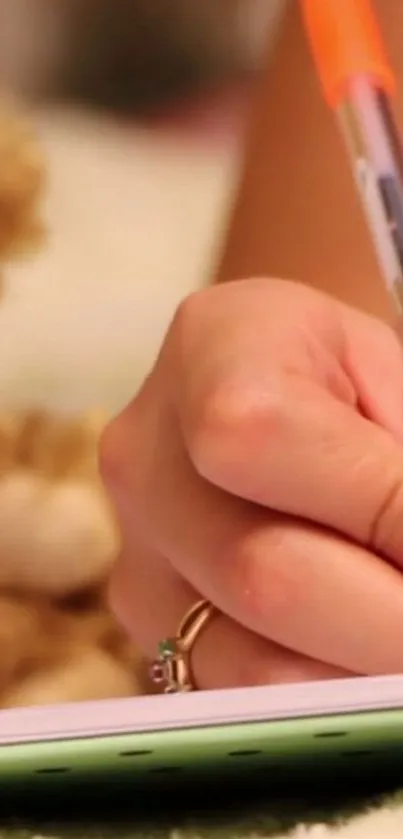 A hand writing in a notebook next to a teddy bear.