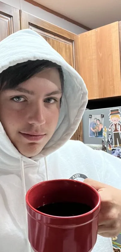 Person in white hoodie holding red coffee mug in kitchen wallpaper.