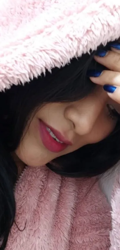 Woman in cozy pink hood with stylish look and blue nails.