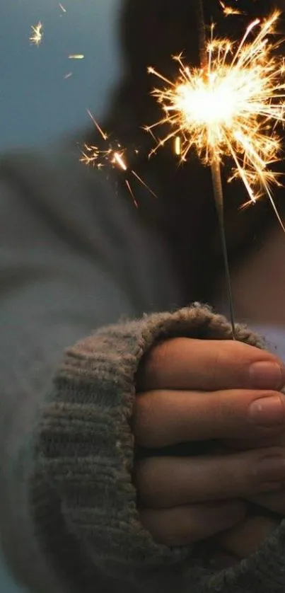 A cozy hand holds a glowing sparkler.