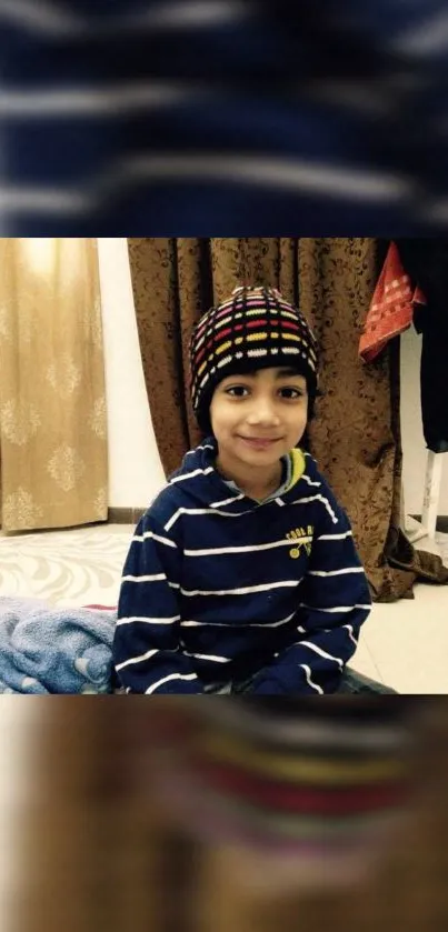 Smiling child in a cozy blue-striped sweater and colorful hat indoors.