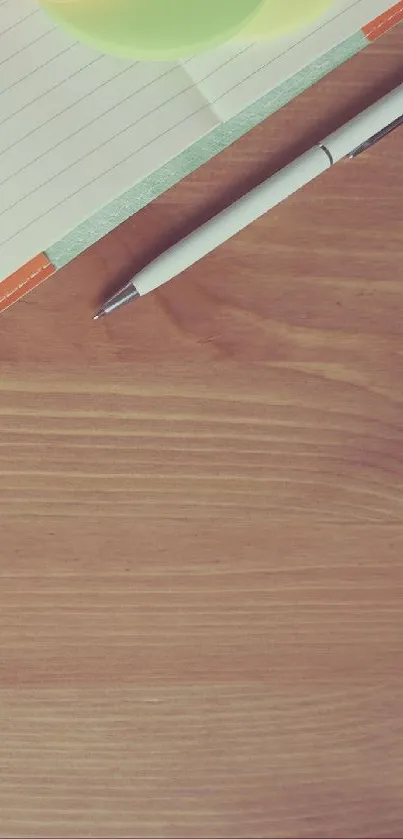 Overhead view of notepad, cup, and plant on wooden desk.