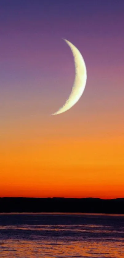 Crescent moon over sunset ocean with an orange sky backdrop.