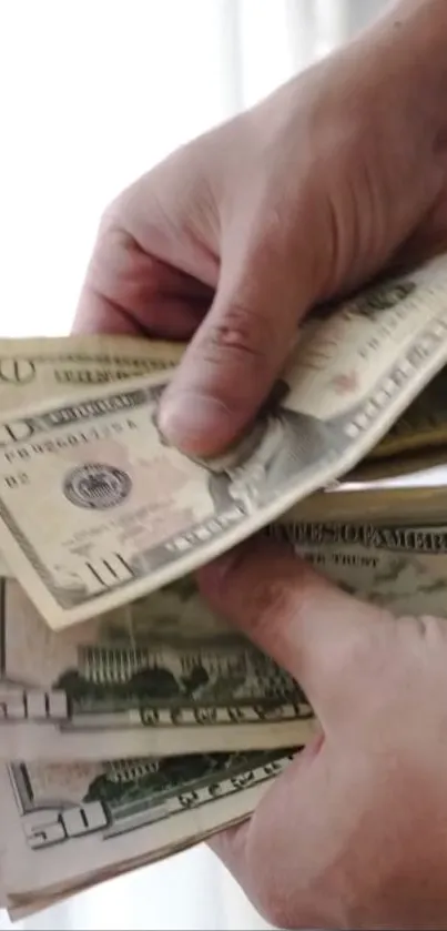 Hands counting dollar bills against light background.