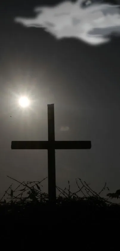 Silhouette of a cross against a dark sunset sky with clouds.