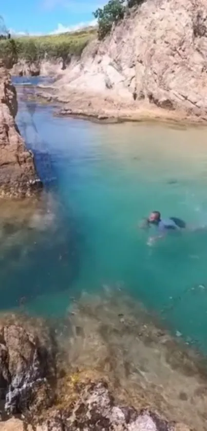 Swimmer in turquoise water by rugged cliffs.