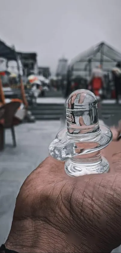 Crystal lingam held in hand against a blurred chaotic background.