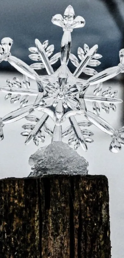 Crystal snowflake sculpture on wooden post against winter backdrop.