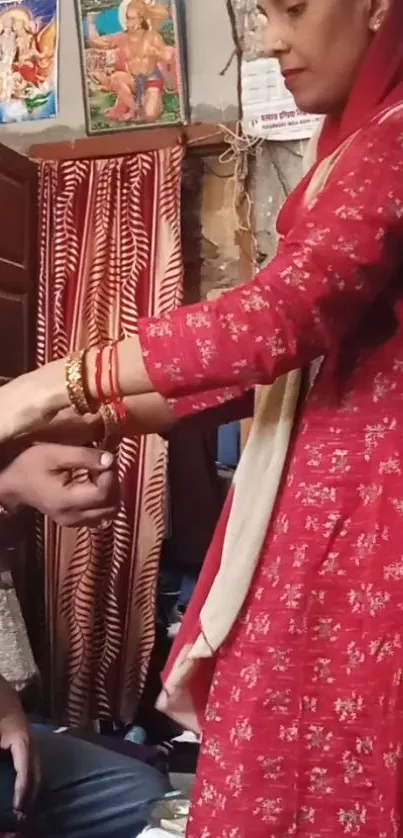 A woman in red tying a Rakhi on a man's wrist in a traditional setting.