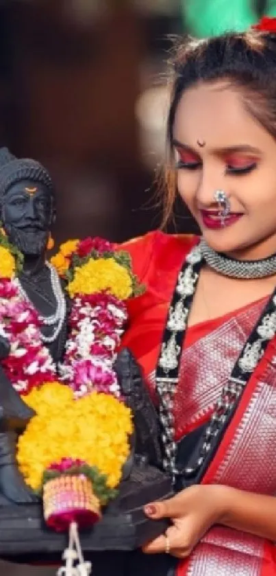 Woman holding a decorated statue in vibrant traditional attire.