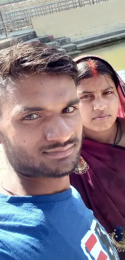 A couple taking a selfie near a serene river with traditional attire.