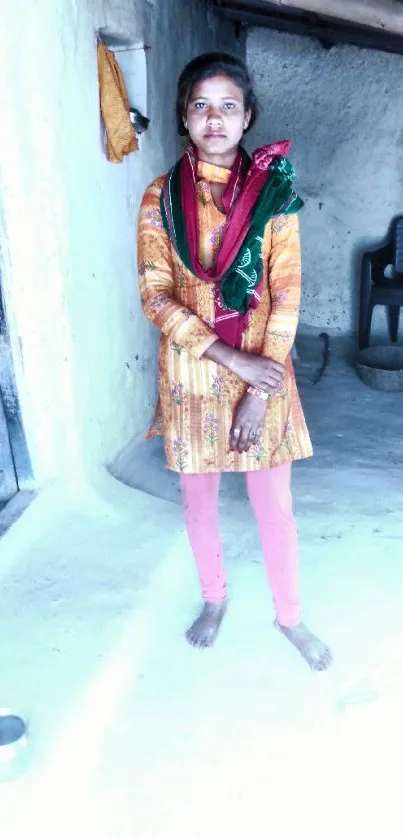 Portrait of a person in traditional attire standing inside a rustic home.