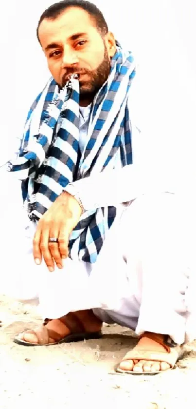 Man squatting in traditional attire with a serene expression and patterned scarf.