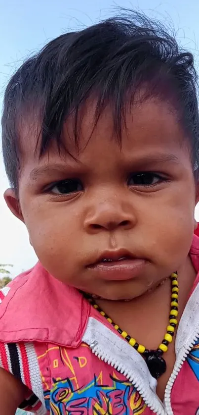 Close-up of a cute baby with vibrant outfit and sky blue background.