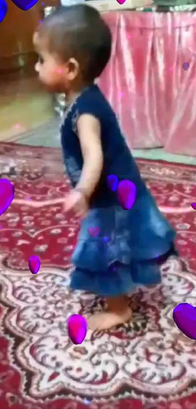 Cute baby girl in blue dress with purple hearts on red carpet.