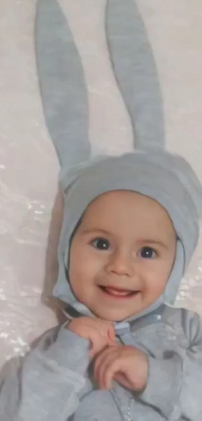 Smiling baby in grey bunny ear hat with light background.