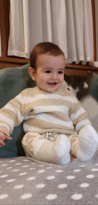 Adorable baby in a beige striped sweater sitting happily.