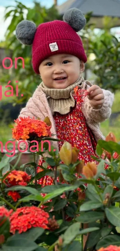 Smiling baby with red hat in a colorful flower garden.