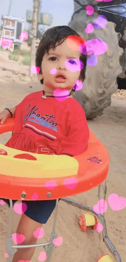 Adorable baby in a red outfit surrounded by pink hearts outdoors.