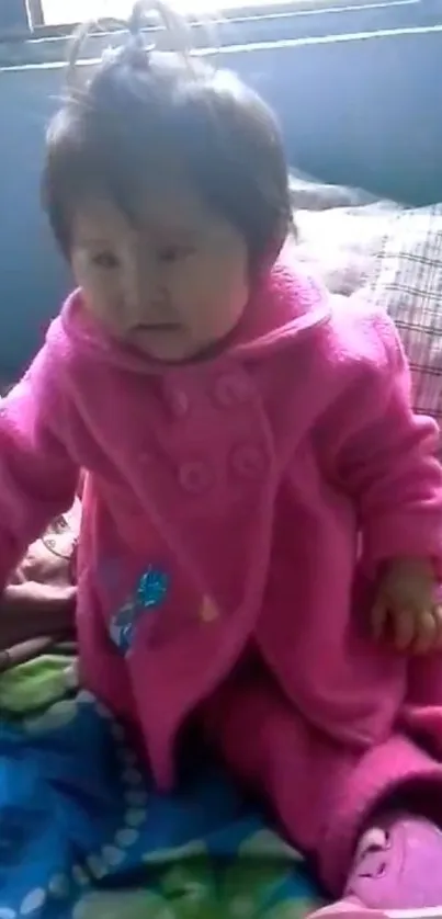 Cute baby in pink coat sitting indoors.