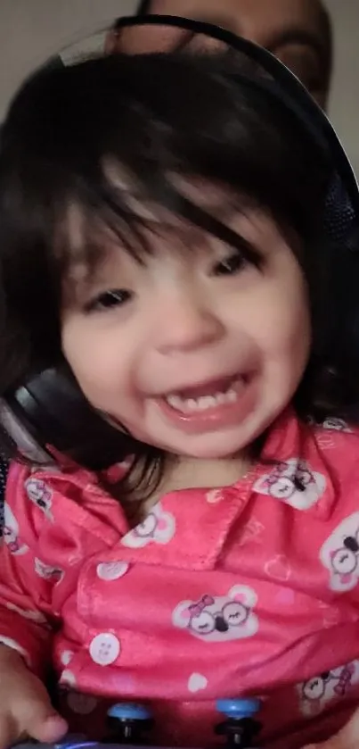 Smiling baby in pink pajamas wearing headphones, joyful expression.