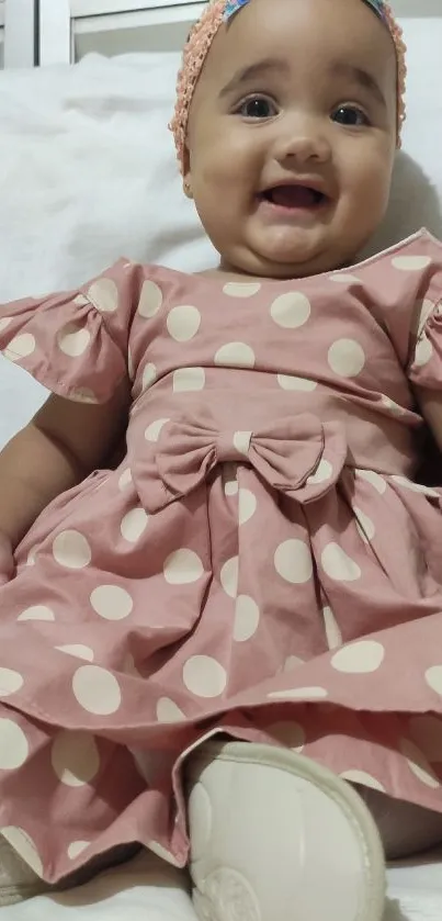 Adorable baby in pink polka dot dress, smiling happily.