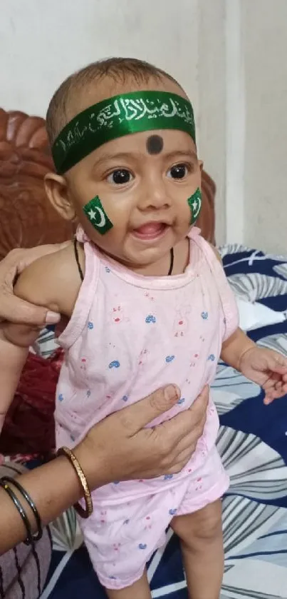 Cute baby smiling with green accessories and patterned bedding.