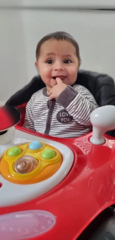 Smiling baby in a red toy car with colorful buttons.