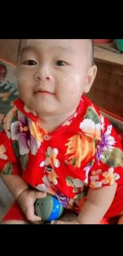 Baby in red floral shirt playing joyfully.