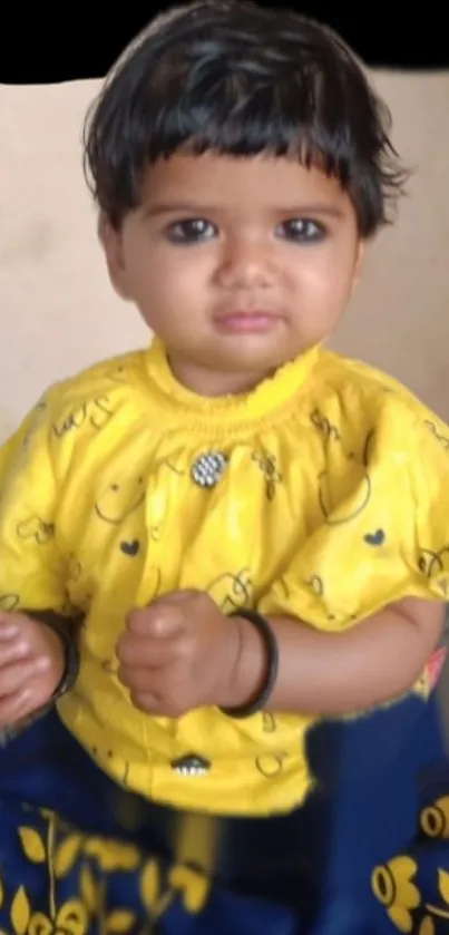 Adorable baby wearing a bright yellow top and smiling.