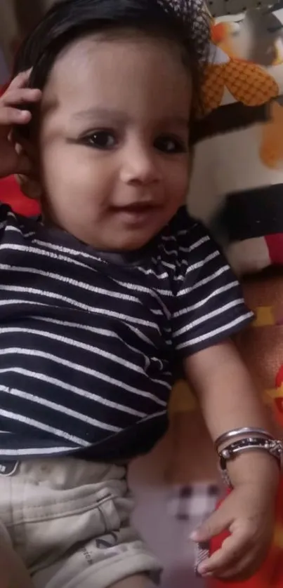 Smiling baby in striped outfit on a colorful cushion.