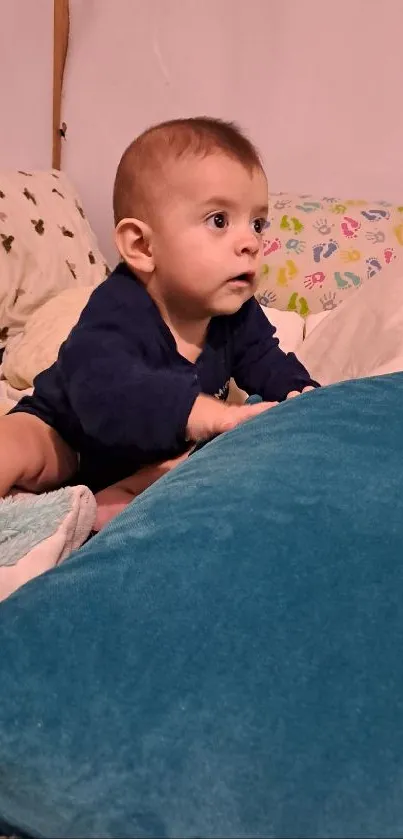 Cute baby sitting on a bed with colorful pillows and teal blue accents.