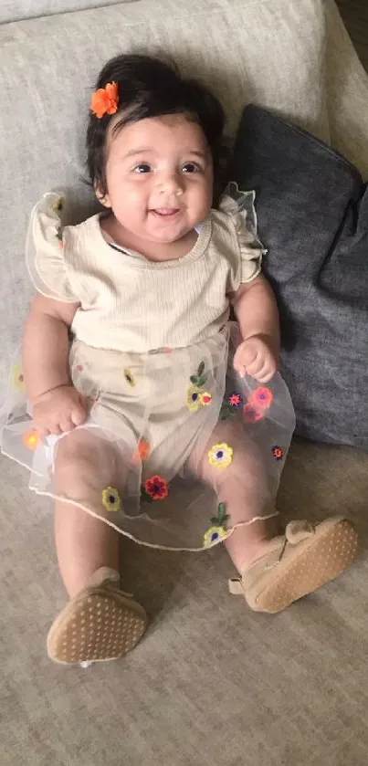 Smiling baby in floral dress on a beige couch.