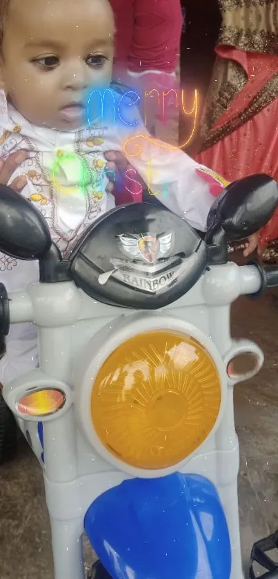 Cute baby in festive attire on a toy motorcycle.