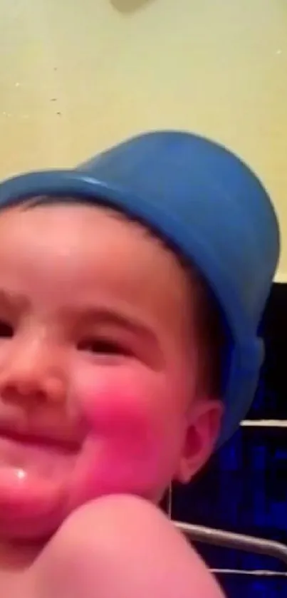 Smiling baby wearing a blue hat with rosy cheeks and a cute expression.