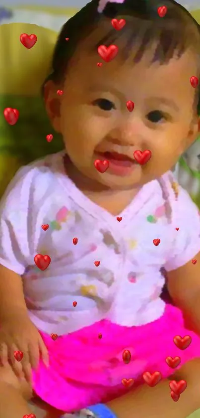 Adorable baby smiling with floating red hearts on a vibrant wallpaper.