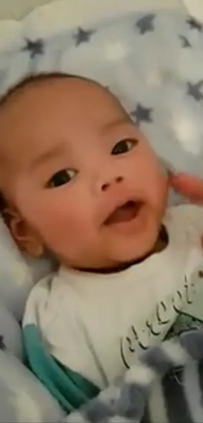 Adorable baby in a blue star-patterned blanket looking cheerful.