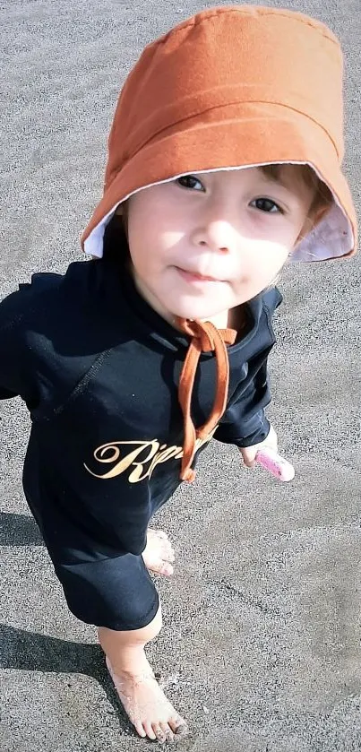 Adorable baby with orange hat on sandy beach.