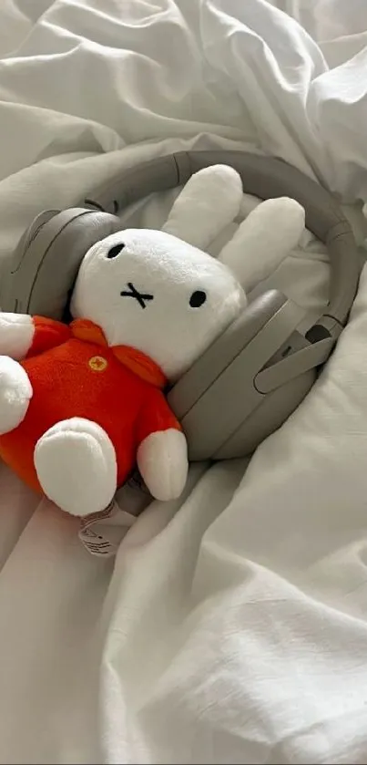 Plush bear with headphones on white blanket.